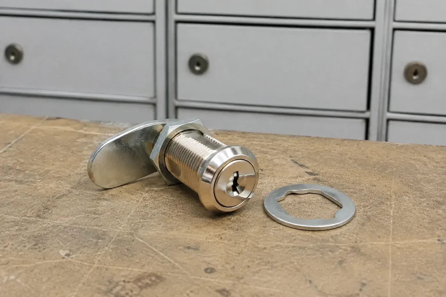 Detached threaded cam lock and mounting washer on a workbench in front of closed mail compartments. — Mailbox Lock Replacement, Newmarket